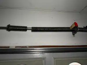 An interior overhead closeup of a coiled metal torsion spring snapped in two with a visible gap separating the sections, illustrating the ultimate result of ignored signs your garage door springs are about to fail.