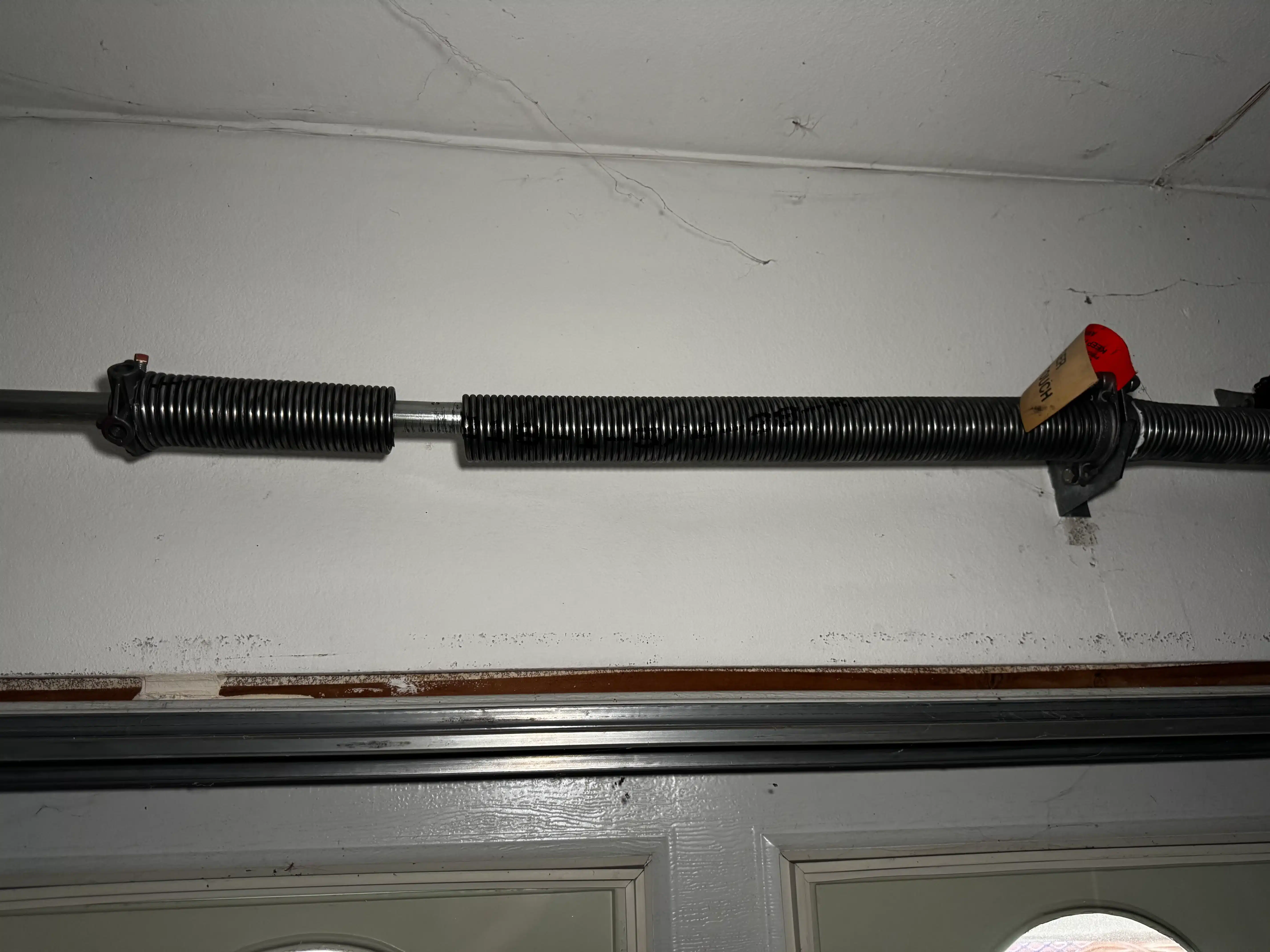An interior overhead closeup of a coiled metal torsion spring snapped in two with a visible gap separating the sections, illustrating the ultimate result of ignored signs your garage door springs are about to fail.