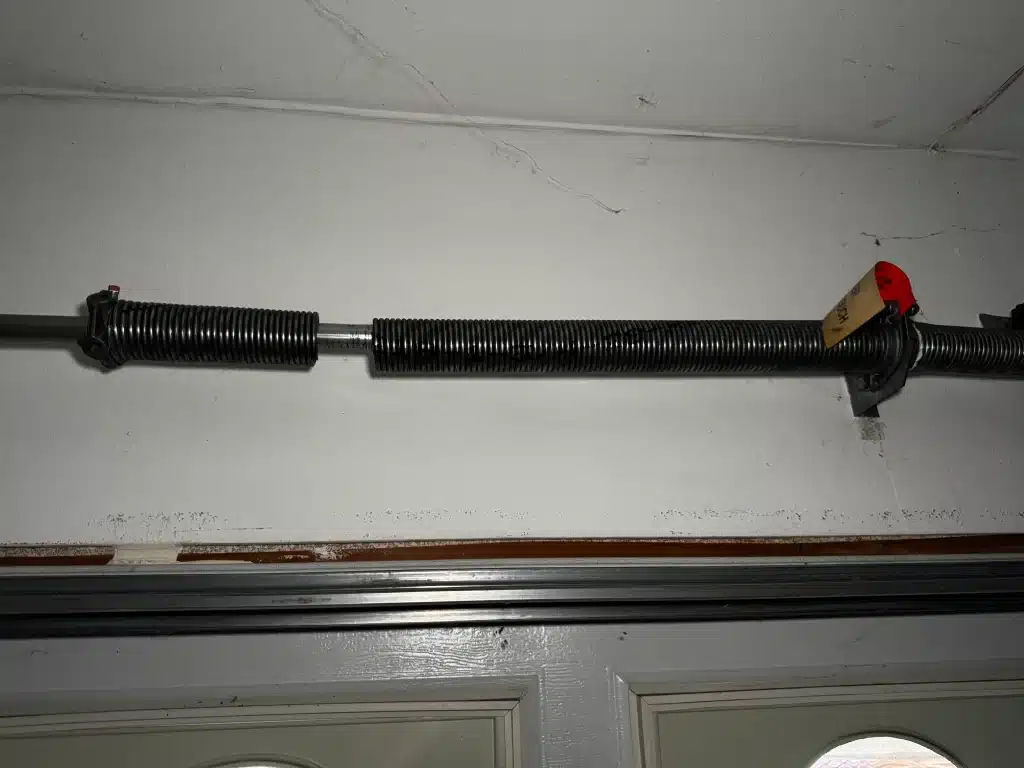An interior closeup of a overhead torsion spring cleanly snapped with a clear gap in the center, providing a direct visual of what causes garage door springs to break.