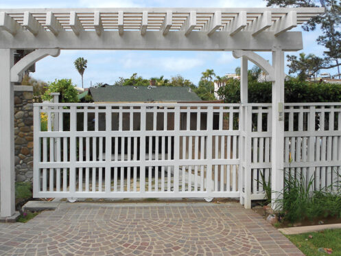 White wooden sliding driveway gate with pergola in a landscaped residential entrance.